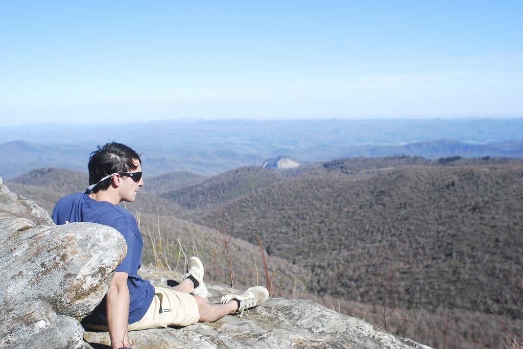 man sitting on rock overlooks mountains