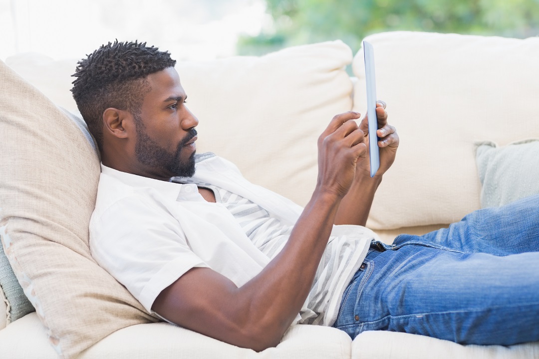 man laying on couch looking at ipad
